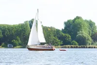 Sailboat "Custom Scalar 28" from 1977 on a serene lake with lush green trees.