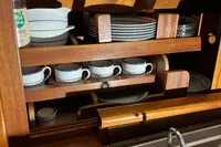Wooden kitchen cabinet with neatly arranged dishes and cups above a stainless steel sink.