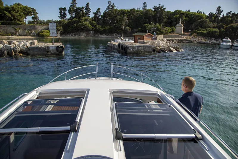  Yacht Photos Pics Nimbus 305 Coupe 2025 cruising near a scenic harbor with lush greenery.