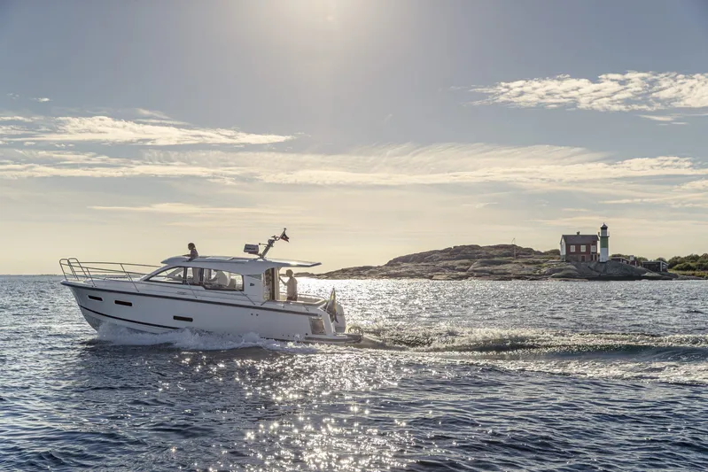  Yacht Photos Pics Nimbus 305 Coupe 2025 cruising near a scenic lighthouse on a sunny day.