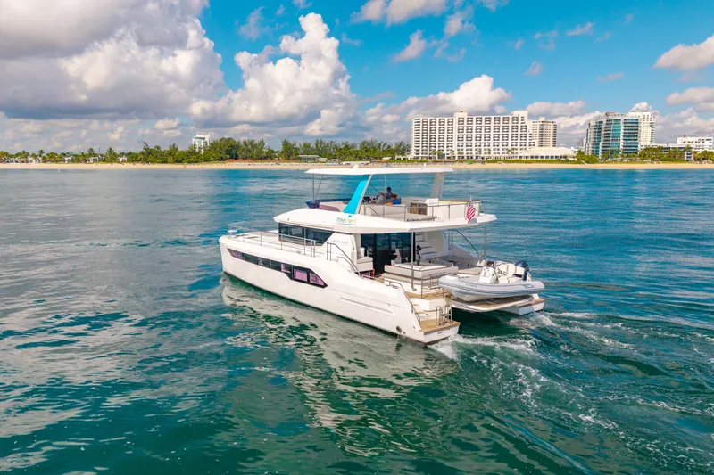 Freedom Yacht Photos Pics 2022 Leopard 53 Powercat cruising near a coastal cityscape under a partly cloudy sky.
