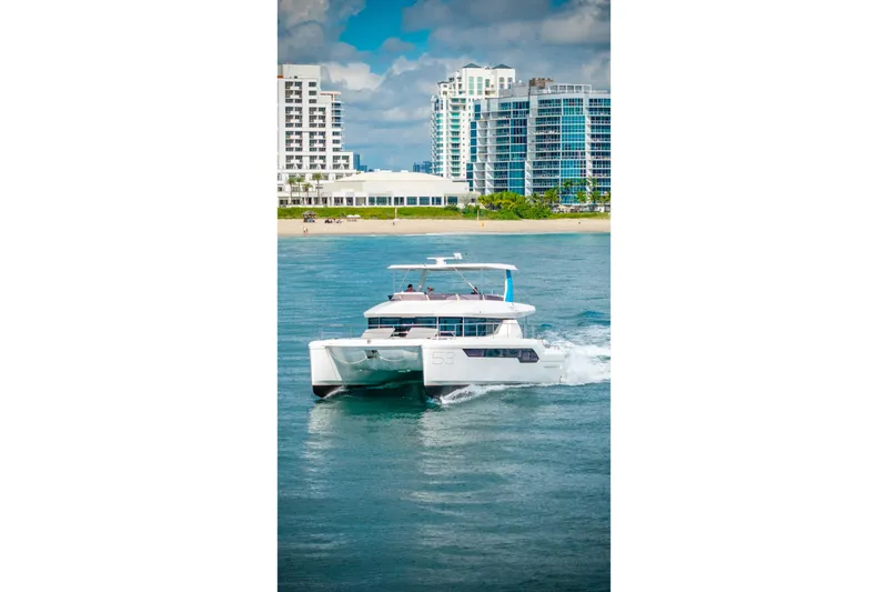 Freedom Yacht Photos Pics 2022 Leopard 53 Powercat cruising near modern beachfront buildings.