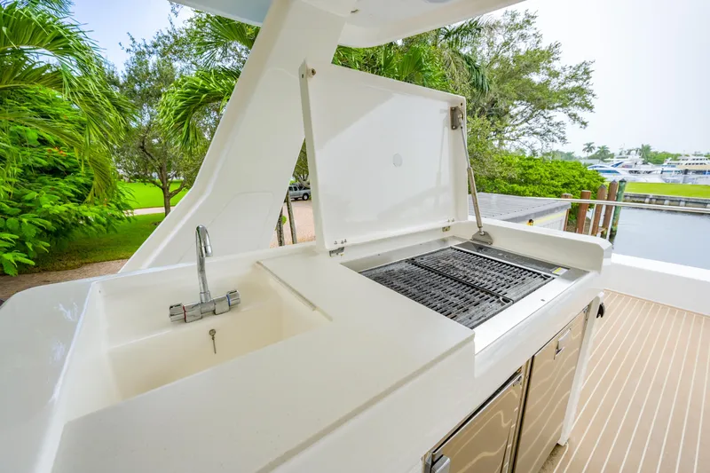 Freedom Yacht Photos Pics Outdoor kitchen on 2022 Leopard 53 Powercat yacht with grill and sink, surrounded by lush greenery.