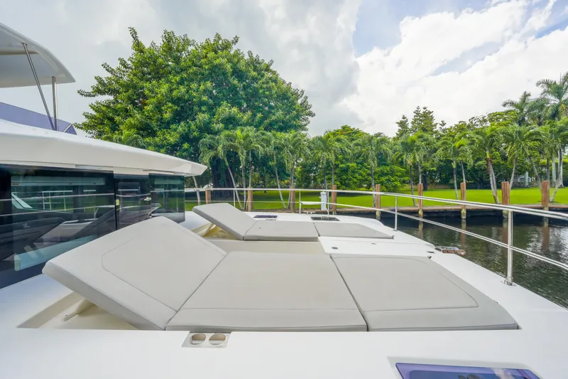 Freedom Yacht Photos Pics Luxurious 2022 Leopard 53 Powercat yacht with sun loungers, docked near lush greenery.