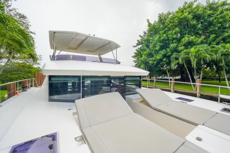 Freedom Yacht Photos Pics 2022 Leopard 53 Powercat yacht with sun loungers, docked near lush greenery.