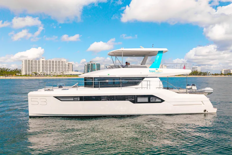 Freedom Yacht Photos Pics 2022 Leopard 53 Powercat yacht cruising near coastal buildings under a blue sky.