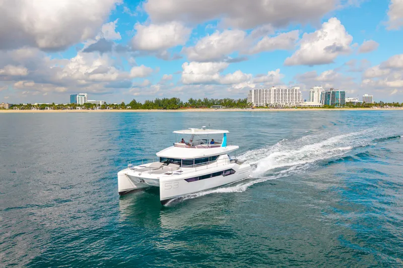 Freedom Yacht Photos Pics 2022 Leopard 53 Powercat cruising near a coastal city under a partly cloudy sky.