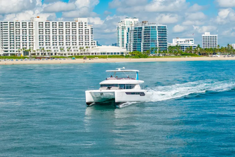 Freedom Yacht Photos Pics 2022 Leopard 53 Powercat cruising near beachfront cityscape under blue skies.