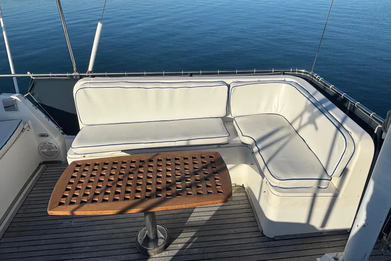 Maximon Yacht Photos Pics 1989 Grand Banks 46 yacht deck with cushioned seating and wooden table, overlooking calm water.