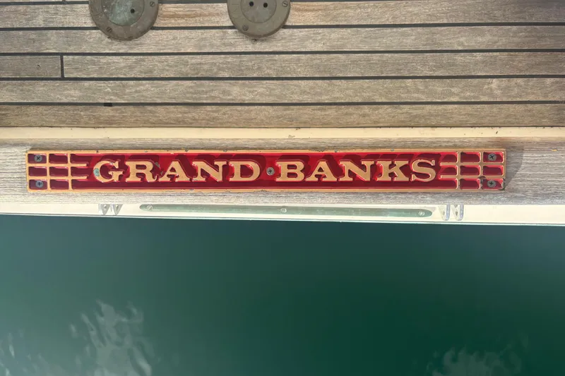 Maximon Yacht Photos Pics 1989 Grand Banks 46 yacht nameplate on wooden deck, above water.