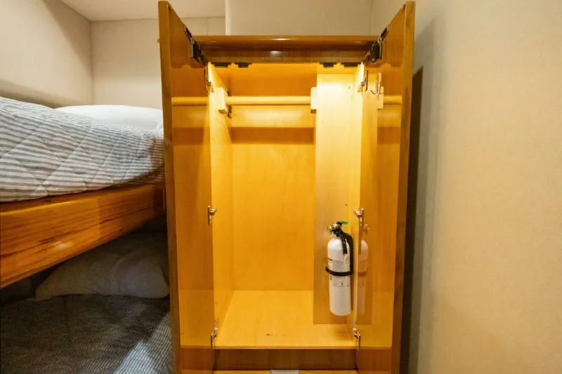 Terrabbean Yacht Photos Pics Open wooden closet with fire extinguisher inside, next to a bed on a 2015 Viking 52 Open.