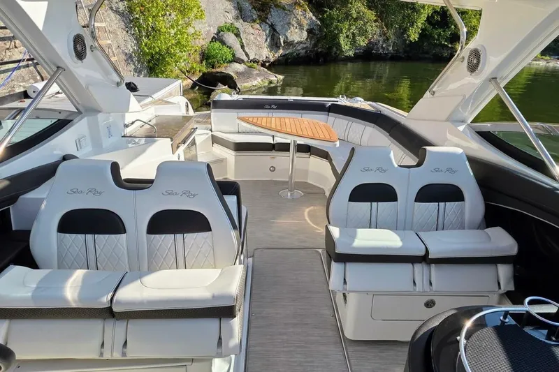  Yacht Photos Pics 2019 Sea Ray 350 SLX boat interior with luxurious seating and table, docked by a scenic shoreline.