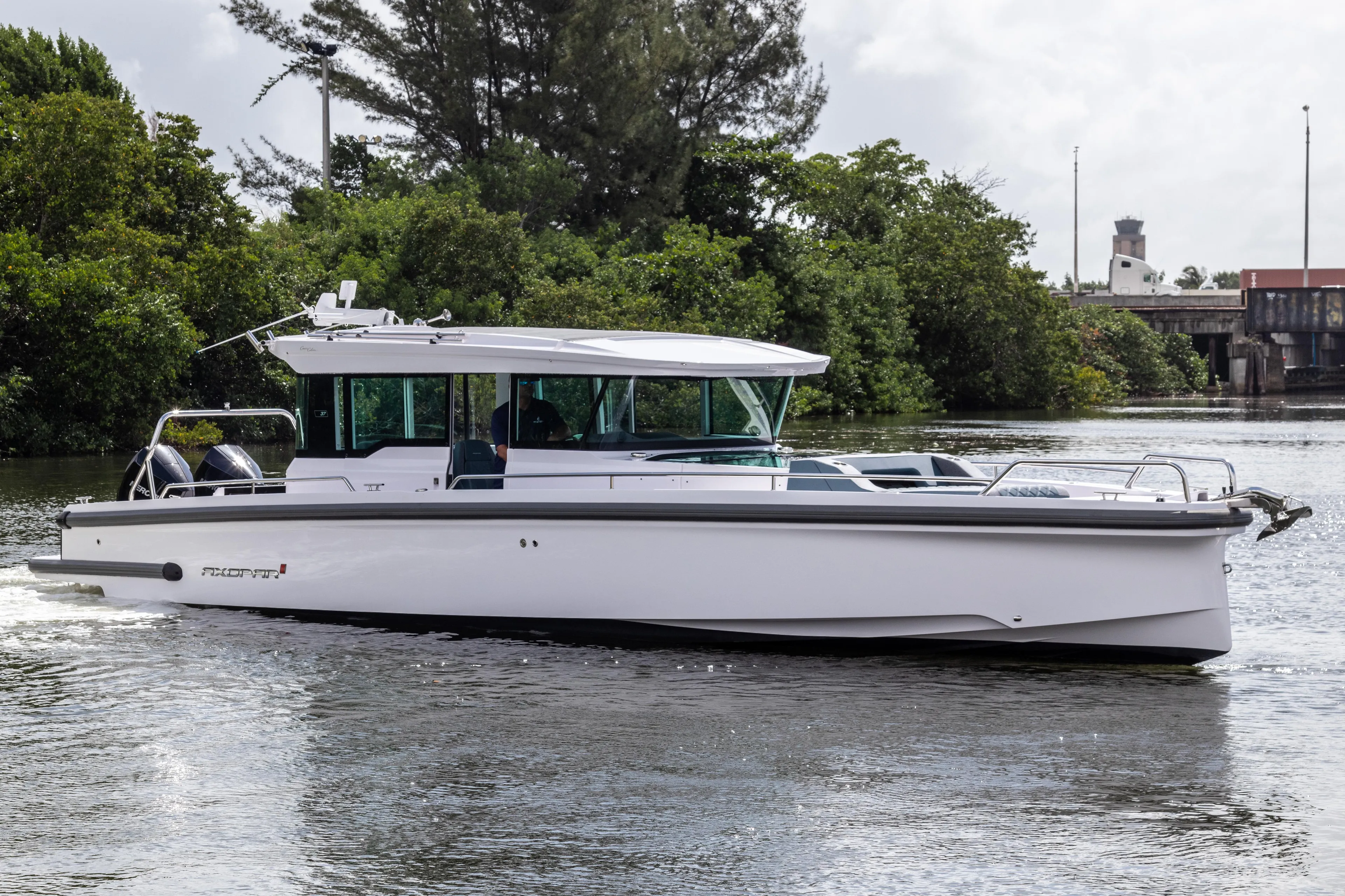 2024 Axopar 37XC CROSS CABIN cruising on a calm river with lush greenery.