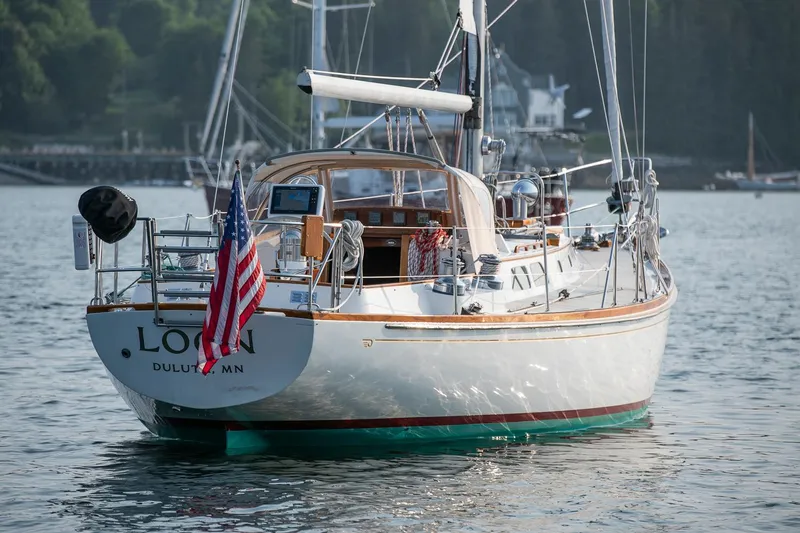 Loon Yacht Photos Pics 1988 Hinckley Sou'wester 42 sailboat on water, displaying American flag, docked near shoreline.