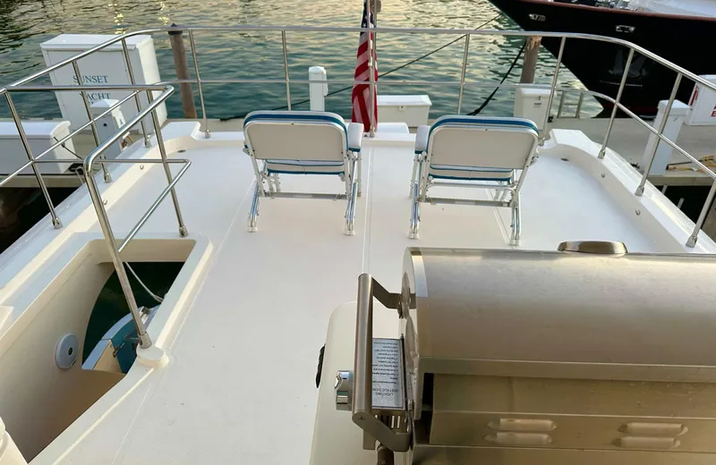 Oasis Yacht Photos Pics 2021 Outer Reef Trident 620 yacht deck with chairs and grill, docked by the water.