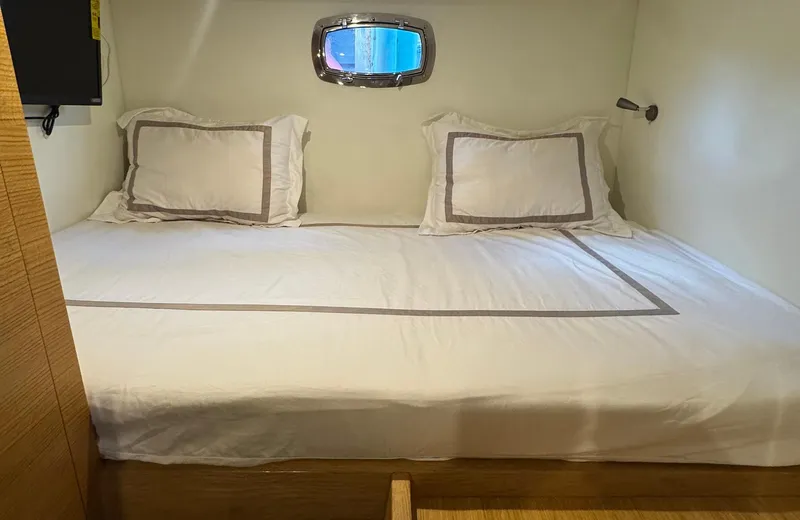 Oasis Yacht Photos Pics Luxurious cabin bed in 2021 Outer Reef Trident 620 yacht, featuring elegant bedding and a porthole window.