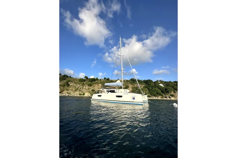 Knotty Cat Yacht Photos Pics 2022 Fountaine Pajot Tanna 47 catamaran anchored near scenic coastline under blue sky.