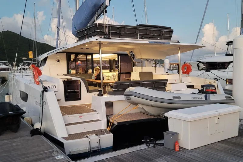 Knotty Cat Yacht Photos Pics 2022 Fountaine Pajot Tanna 47 catamaran docked with inflatable boat and scenic backdrop.