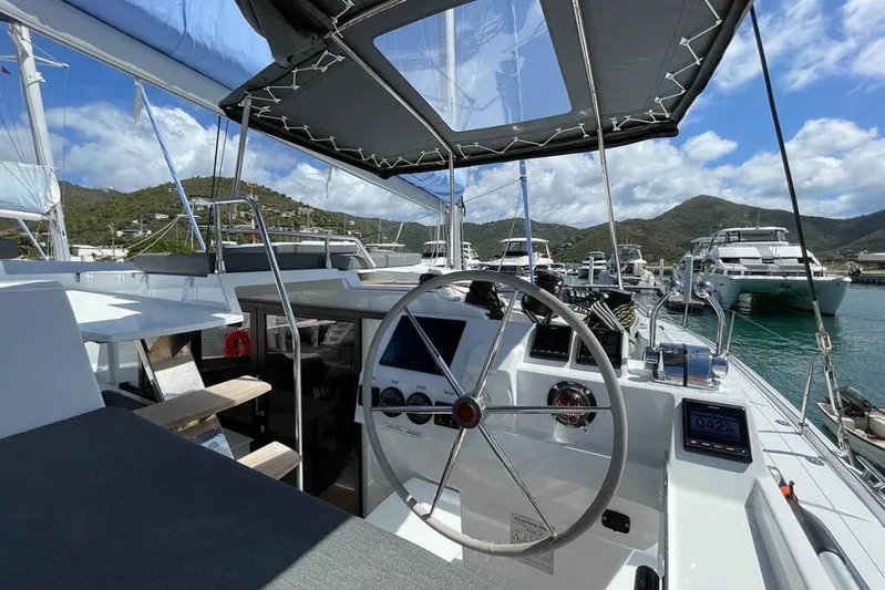 Knotty Cat Yacht Photos Pics 2022 Fountaine Pajot Tanna 47 yacht cockpit with steering wheel, docked in scenic marina.