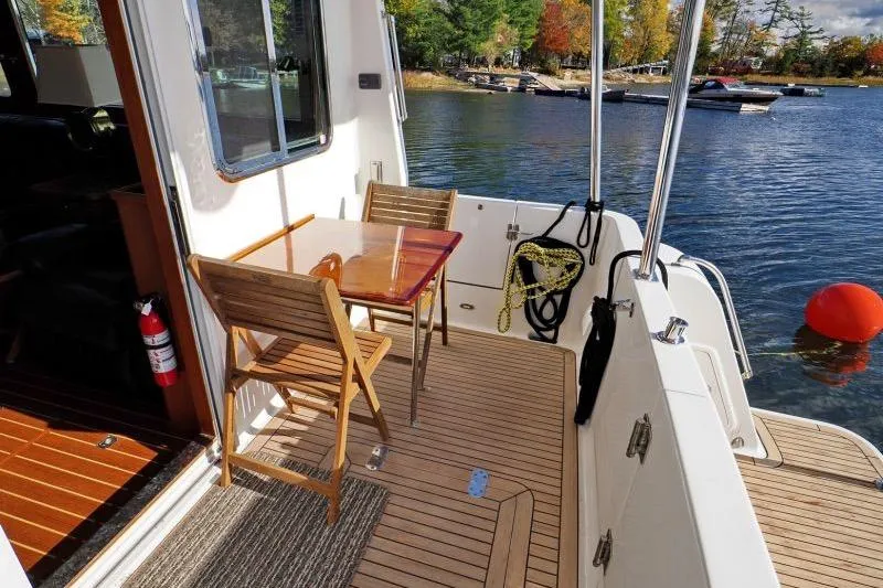 Sharki's Wake Yacht Photos Pics 2016 North Pacific 45 Pilothouse yacht deck with wooden chairs and table by the water.