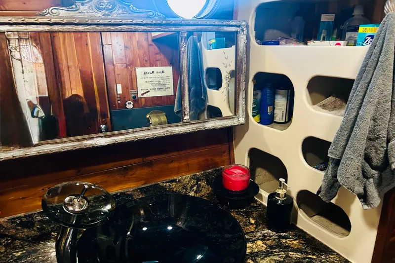 Devil's Gauntlet Yacht Photos Pics Vintage 1977 Custom Brigantine bathroom with ornate mirror, black sink, and storage shelves.