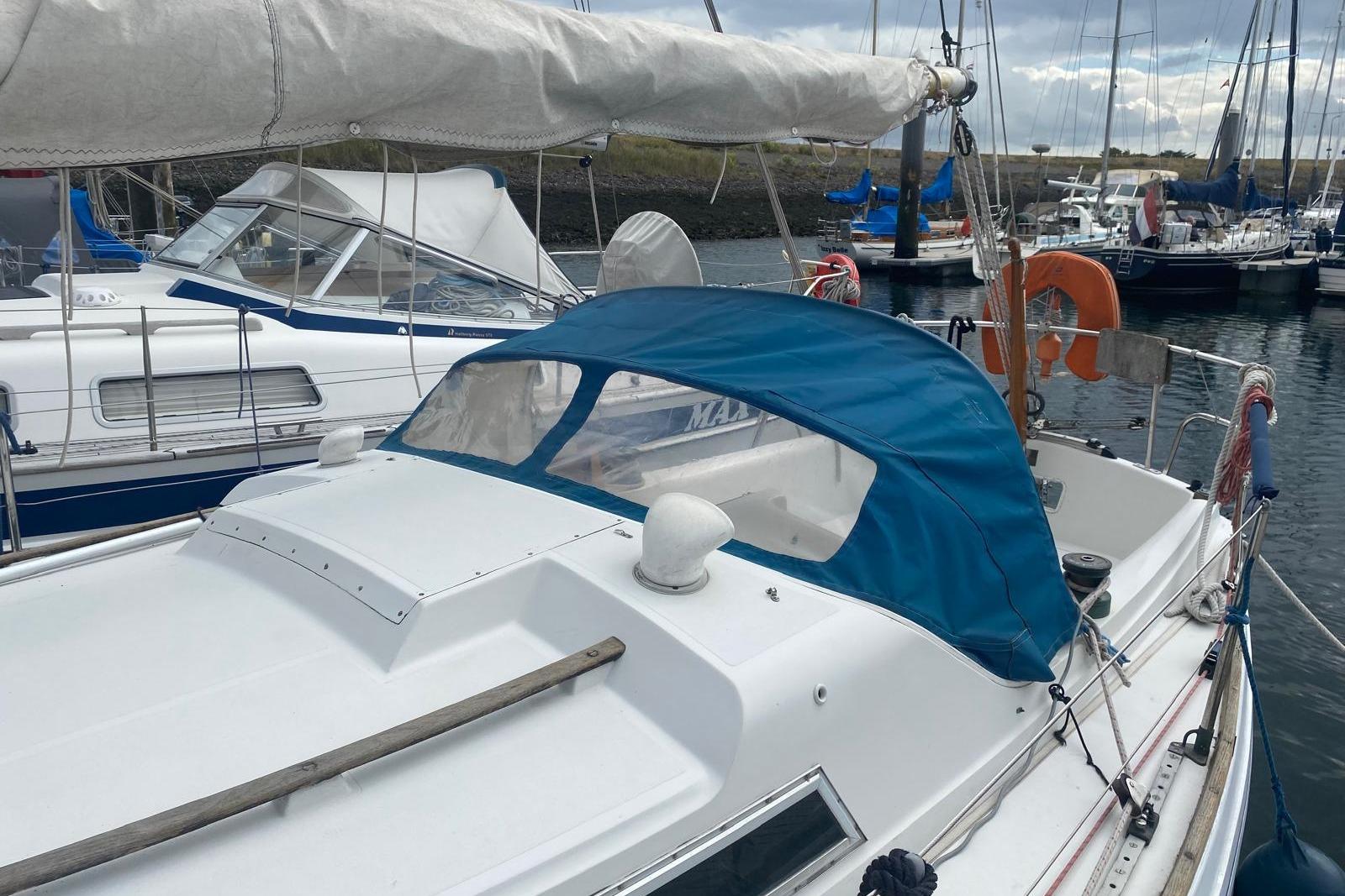 1977 Nicholson 31 sailboat docked in marina, featuring blue canopy and white deck.