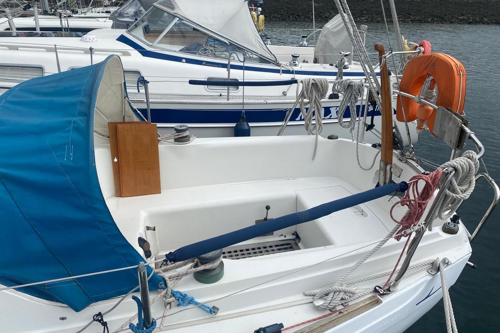 1977 Nicholson 31 sailboat with blue canopy and lifebuoy, docked in marina.