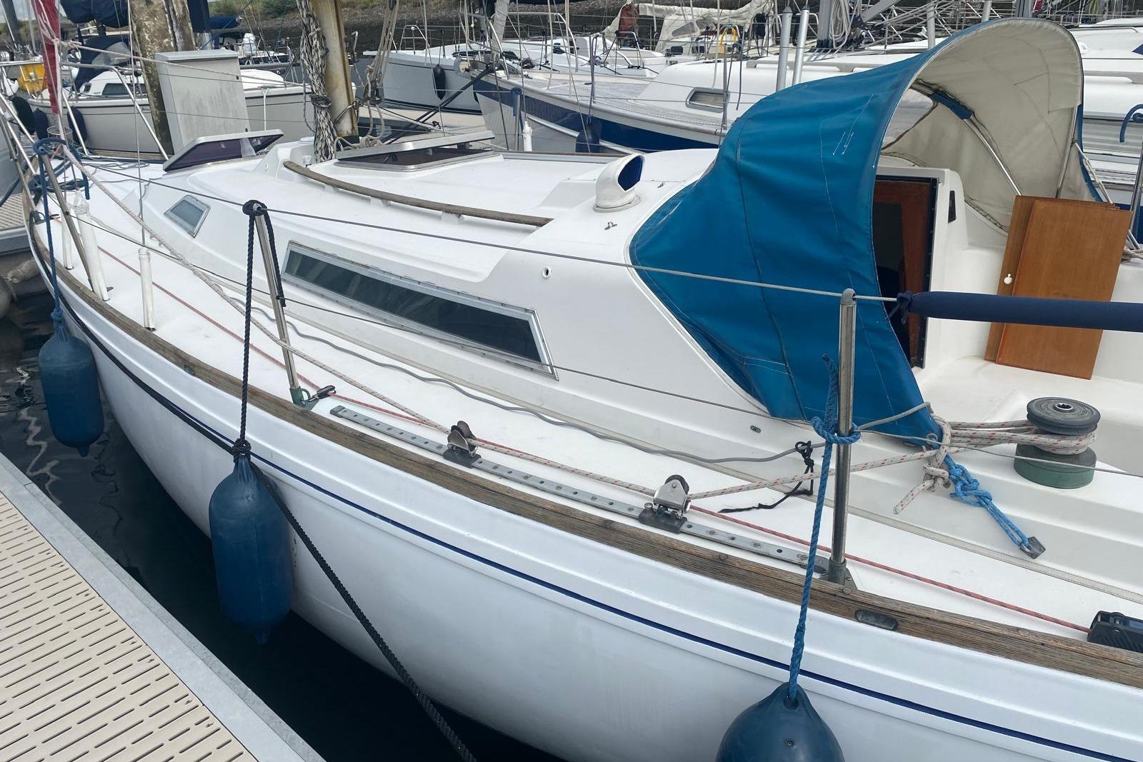 1977 Nicholson 31 sailboat docked, featuring blue canopy and white hull.