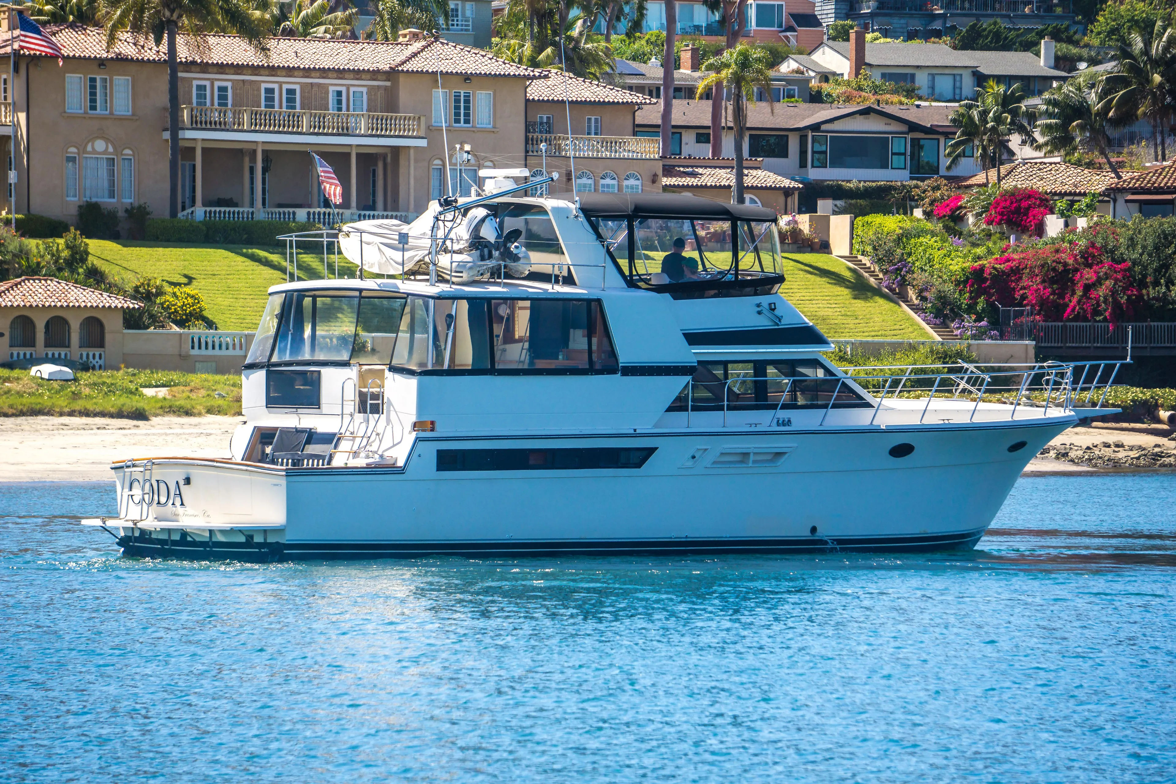 Coda Yacht Photos Pics 1989 Californian 55 Cockpit Motor Yacht on serene water near luxury waterfront homes.
