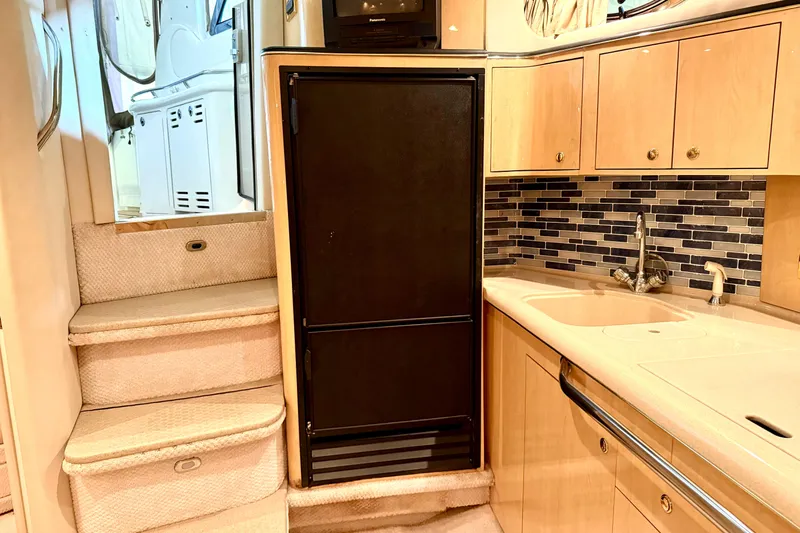 No Tan Lines Yacht Photos Pics Interior of 2000 Sea Ray 410 Sundancer yacht with kitchenette, black fridge, and stairs.