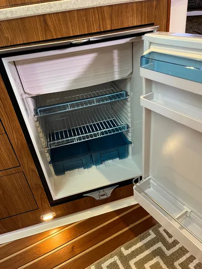  Yacht Photos Pics Open refrigerator inside 2010 Pursuit OS 345 Offshore boat, featuring wooden cabinetry and striped flooring.