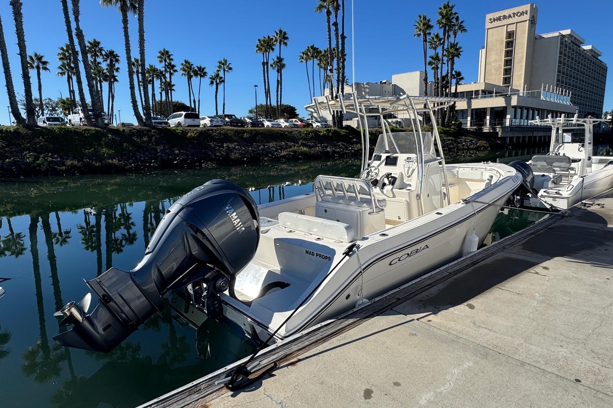 2022 Cobia 237 Center Console boat docked near palm trees and hotel.