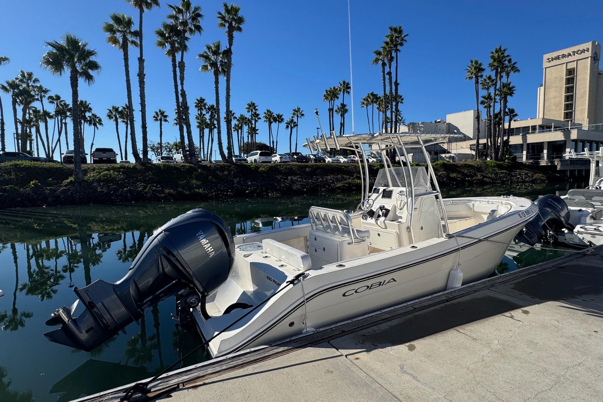 2022 Cobia 237 Center Console boat docked near palm trees and hotel.