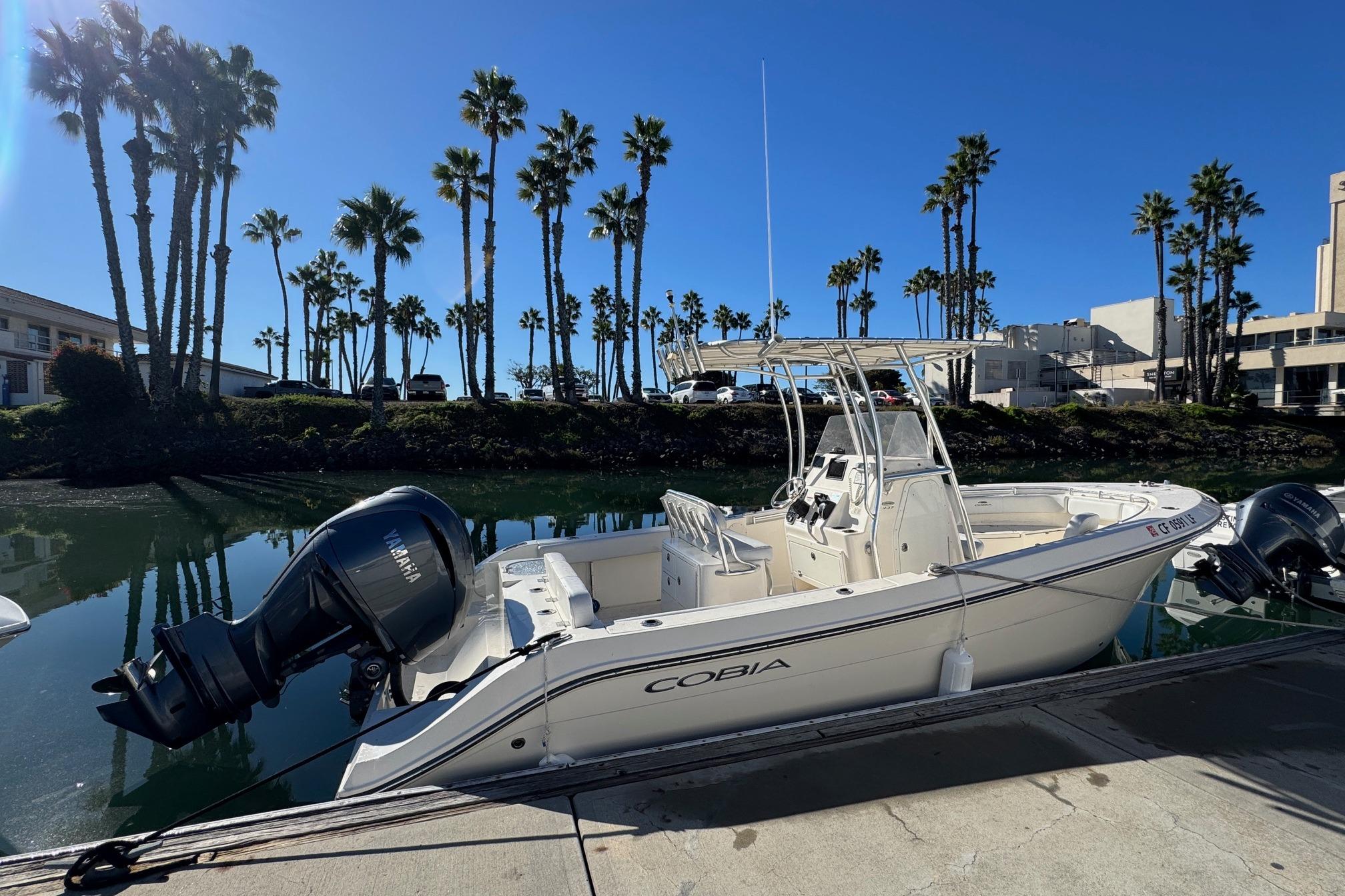 2022 Cobia 237 Center Console boat docked by palm trees under clear blue sky.