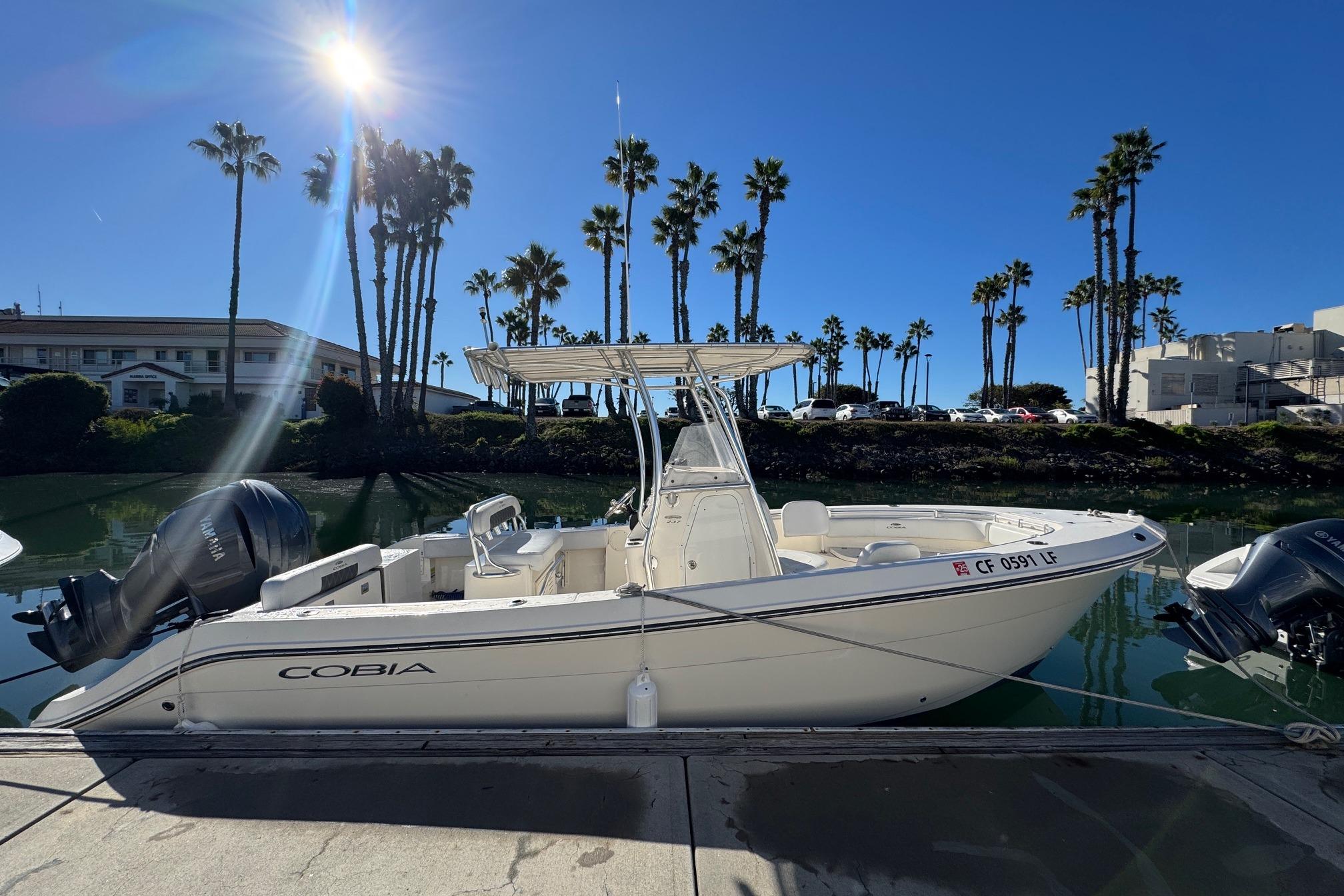 2022 Cobia 237 Center Console boat docked under clear blue sky with palm trees.