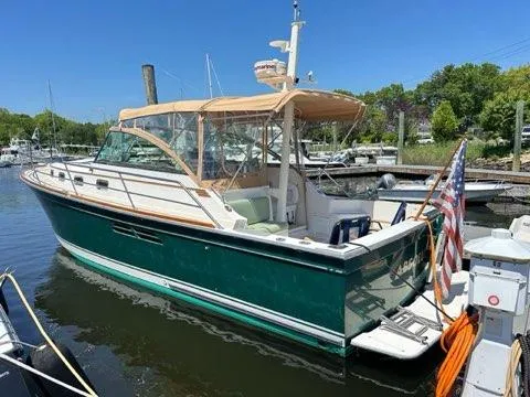  Yacht Photos Pics 1999 Sabreline 36 Express boat docked, green hull, tan canopy, American flag, sunny day.