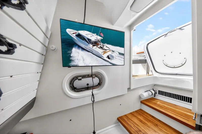 Knot Sorry Yacht Photos Pics 2022 Tiara Yachts 38 LX interior with TV displaying yacht image, wooden steps, and porthole.