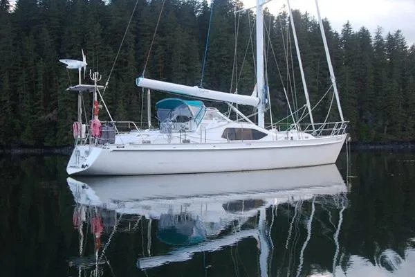 Raynad Yacht Photos Pics Custom Steel Cutter World Cruiser 2000 sailboat on calm water, surrounded by forest.