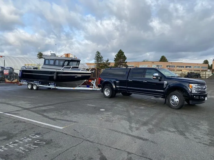  Yacht Photos Pics Black truck towing 2022 custom aluminum fishing boat on trailer in parking lot.