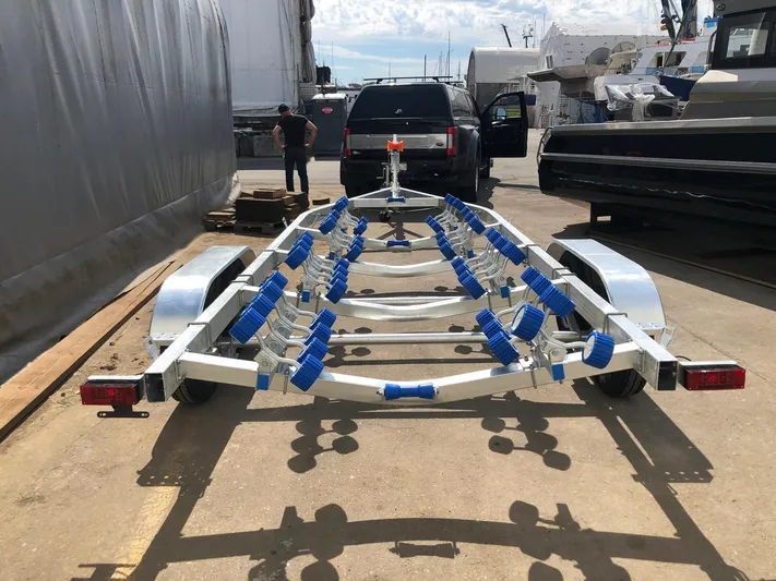  Yacht Photos Pics 2022 Custom Aluminum Fishing trailer with blue rollers, parked outdoors near vehicles and boats.