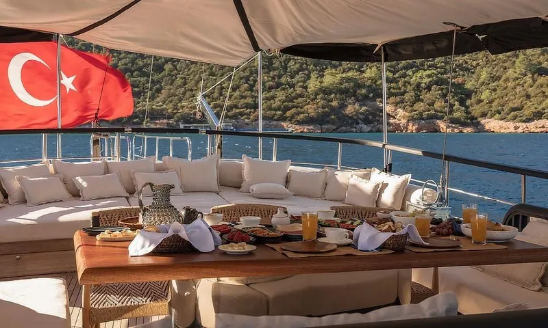 27 M Deluxe Gulet Yacht Photos Pics Luxurious yacht deck with dining setup, Turkish flag, and scenic coastal view.