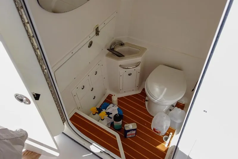  Yacht Photos Pics 2015 Edgewater 320CC boat bathroom with sink, toilet, and cleaning supplies on wooden floor.