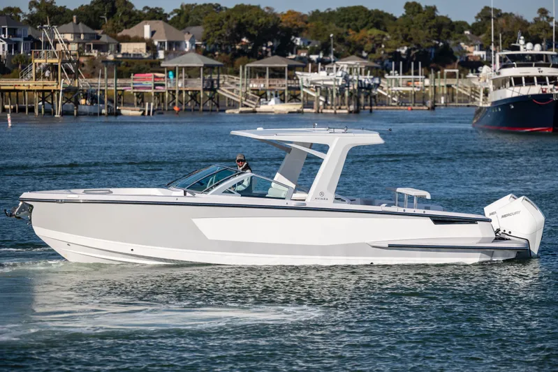  Yacht Photos Pics 2023 Aviara AV32 OB boat cruising on a scenic waterfront with houses in the background.