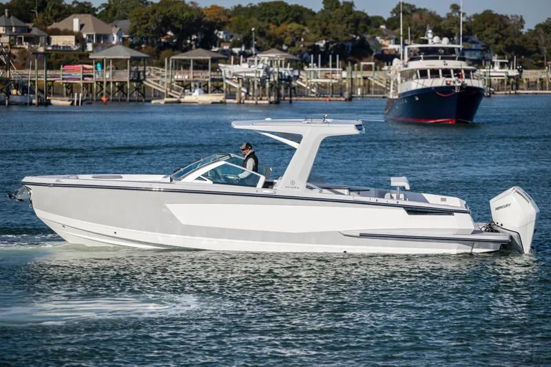  Yacht Photos Pics 2023 Aviara AV32 OB boat cruising on a calm waterway near docks and other boats.