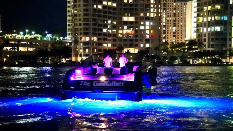The Godfather Yacht Photos Pics VanDutch 55 yacht with vibrant lights on water at night, city skyline in background.
