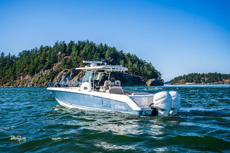  Yacht Photos Pics 2017 Boston Whaler 330 Outrage cruising near a forested island under clear blue skies.