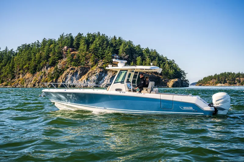  Yacht Photos Pics 2017 Boston Whaler 330 Outrage boat cruising near a forested island.