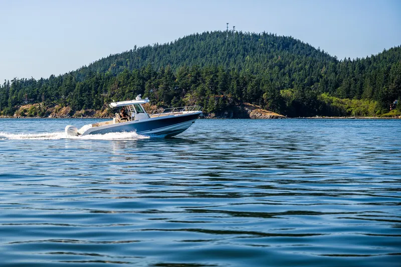  Yacht Photos Pics 2017 Boston Whaler 330 Outrage cruising on a serene lake with forested hills in the background.