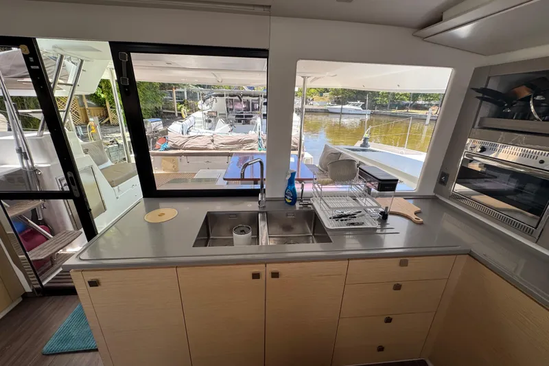 Ten:10 Yacht Photos Pics Interior view of 2017 Fountaine Pajot SABA 50 catamaran kitchen with outdoor deck access.