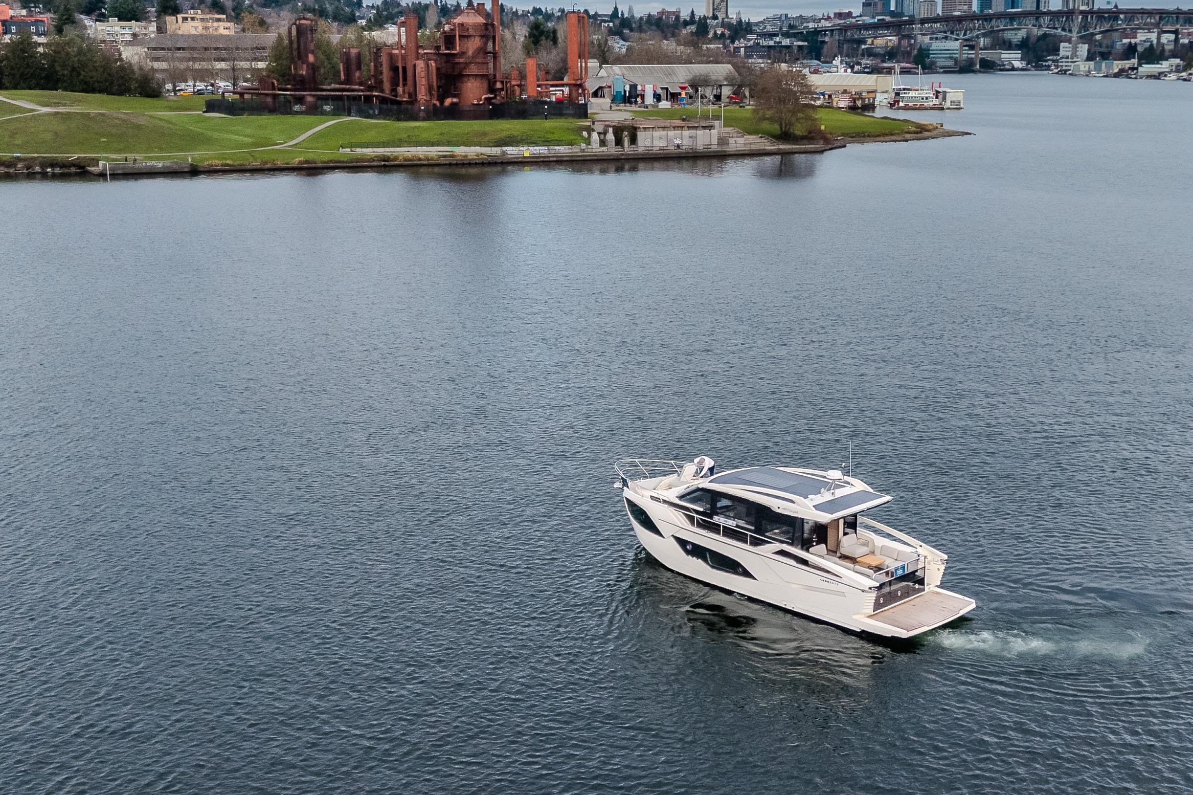 2026 Absolute 48 Coupe yacht cruising on a scenic waterfront with industrial backdrop.
